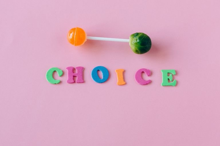 Colorful choice between candy and vegetable on pink background.