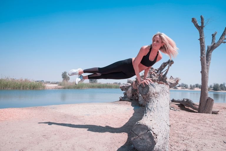 Woman performing an athletic pose on a log by a lake in Dubai's desert landscape.